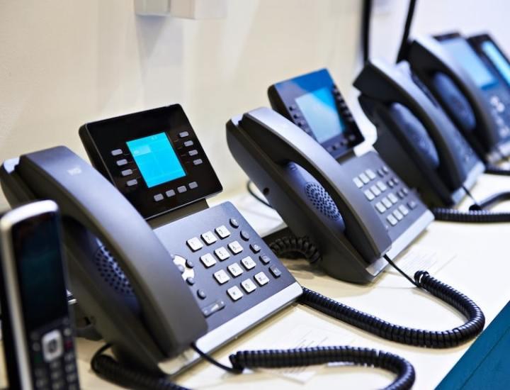 Row of office telephones with digital displays arranged on a desk.