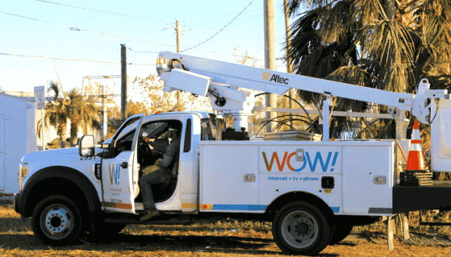 WOW! internet, TV, and phone service truck with a bucket lift parked on a sunny day, with a technician sitting in the driver's seat