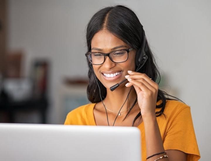 Smiling woman wearing glasses and a headset, working on a laptop