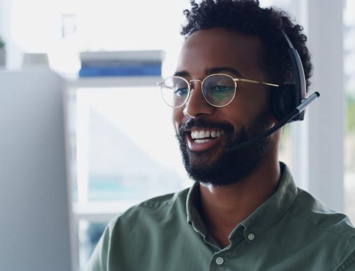 Smiling customer service representative with glasses and a headset working at a computer.