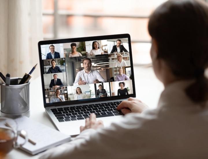 Person participating in a video conference call on a laptop with multiple people displayed on the screen.