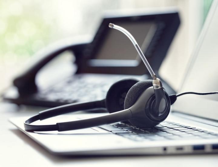 Headset resting on a laptop keyboard with a telephone in the background.